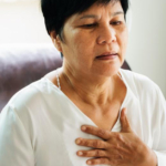 An Asian woman holding onto her chest, experiencing chest pains with heart disease.