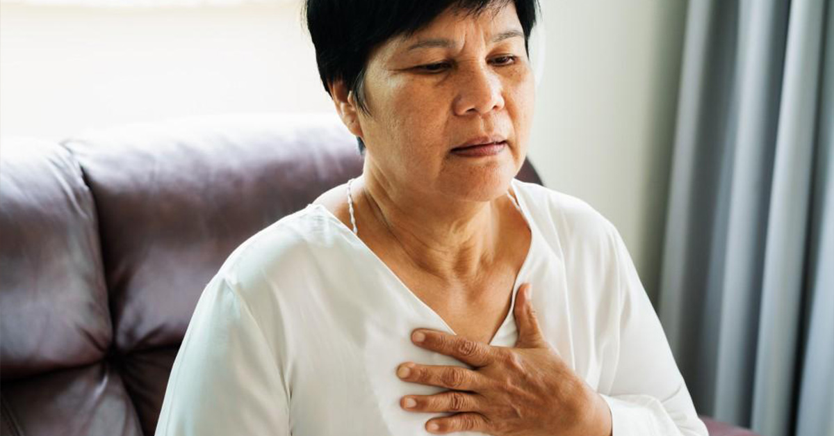 An Asian woman holding onto her chest, experiencing chest pains with heart disease.